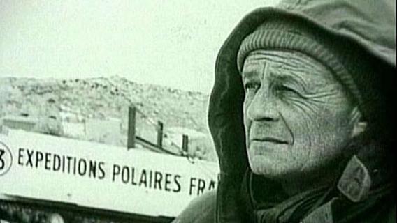 Photo en noir et blanc montrant Paul- Emile Victor de profil, habillé en tenue polaire, avec en fond un fronton de bâtiment où il est indiqué "Expéditions polaires françaises". 