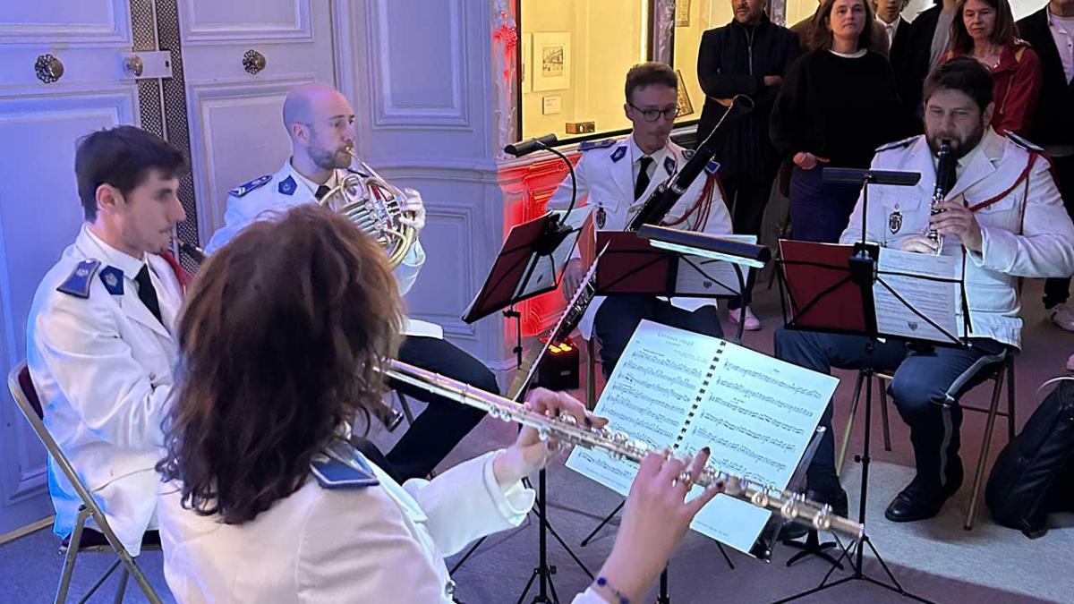 Quintette de La Musique des gardiens de la paix. 5 musiciens d'instruments à vent sont en demi-cercle devant un public debout. Ils portent un uniforme blanc.