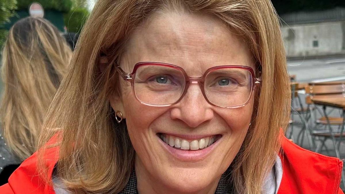 Portrait serré de Léa Fazer  très souriante. Elle porte des cheveux blonds mi-longs, des lunettes et un manteau rouges..