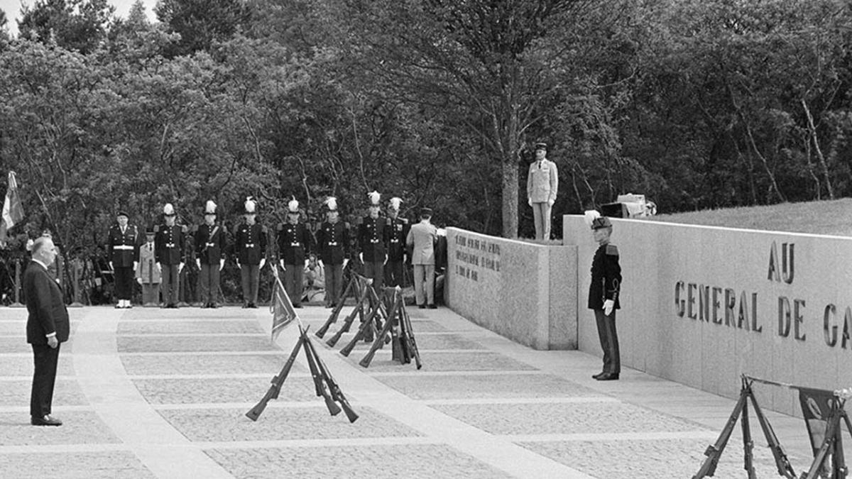 Photo en noir et blanc qui montre George Pompidou dans un recueil officiel devant le monument à la mémoire du général. Il pose très raide et est entouré de soldats en uniformes d'apparat au garde-à-vous. 