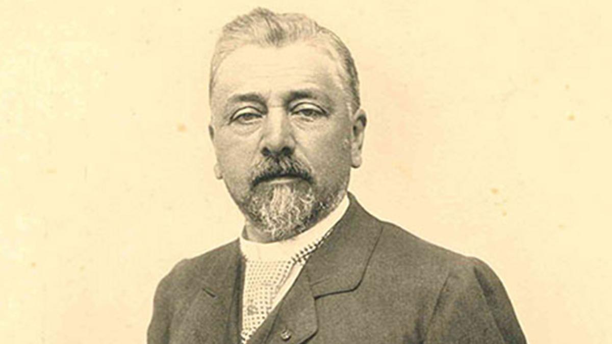 Photo portrait en couleur sépia de Gustave Eiffel. Il porte une barbiche grisonnante et des cheveux courts. Il ne sourit pas. 