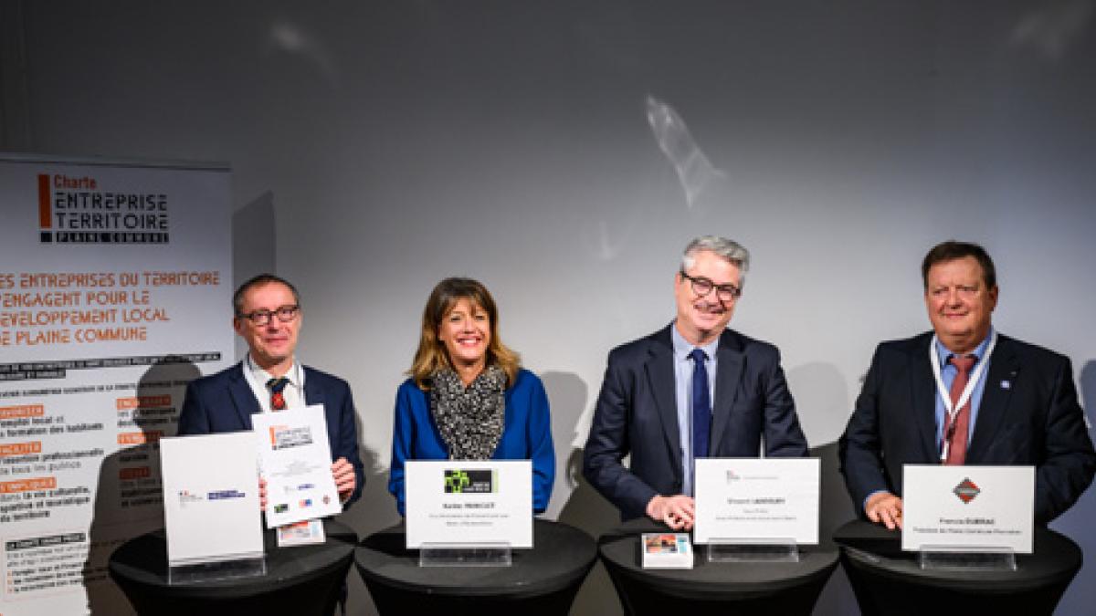 Signature de la charte. Les 4 signataires de la charte sont alignés. Ils posent en présentant devant eux le document signé.