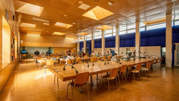 Photographie de la salle de lecture des ANOM avec tables de consultation et lecteurs au premier plan et l'oeuvre de François Seigneur au second plan