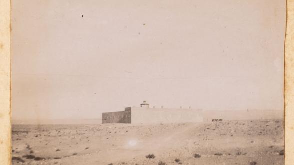Image ancienne d'un bâtiment isolé dans le désert, avec un ciel clair et des dunes de sable