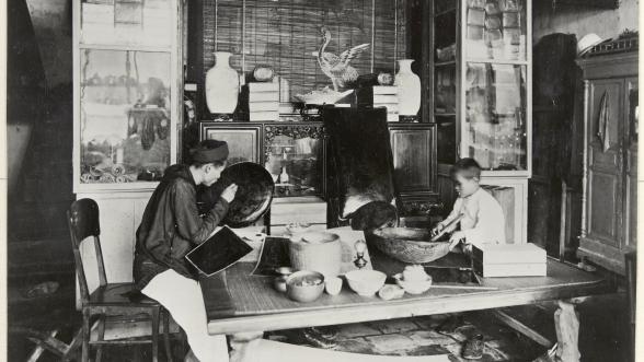 Photographie en noir et blanc de l'intérieur de l'atelier d'un laqueur avec un laqueur travaillant et un enfant 