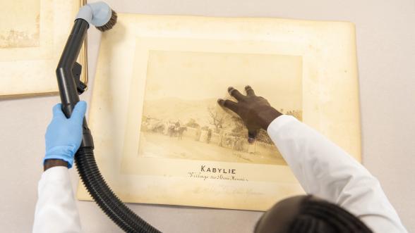 Photographie en plongée d'une archiviste dépoussierant un document d'archive.