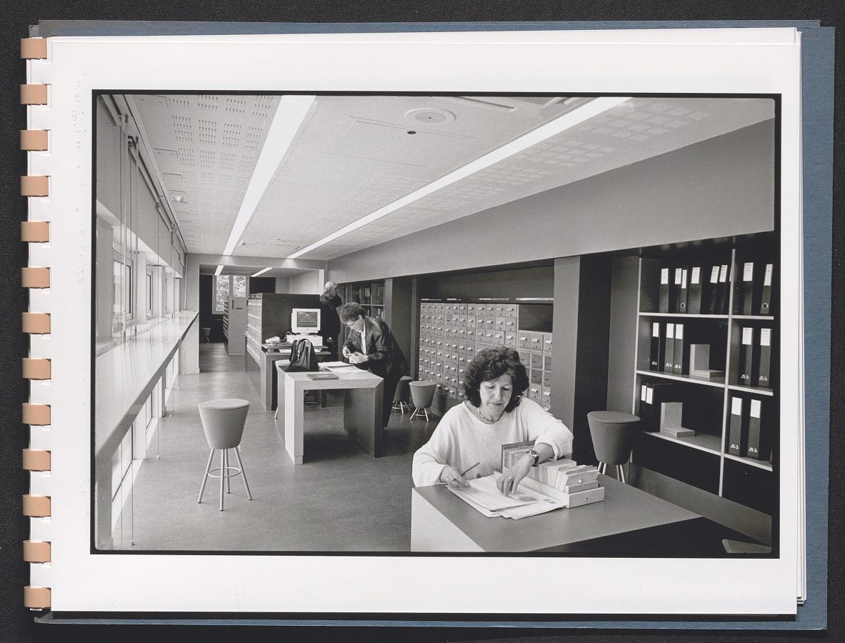 Photographie en noir et blanc représentant une personne consultant un inventaire d'archives dans la salle des inventaires