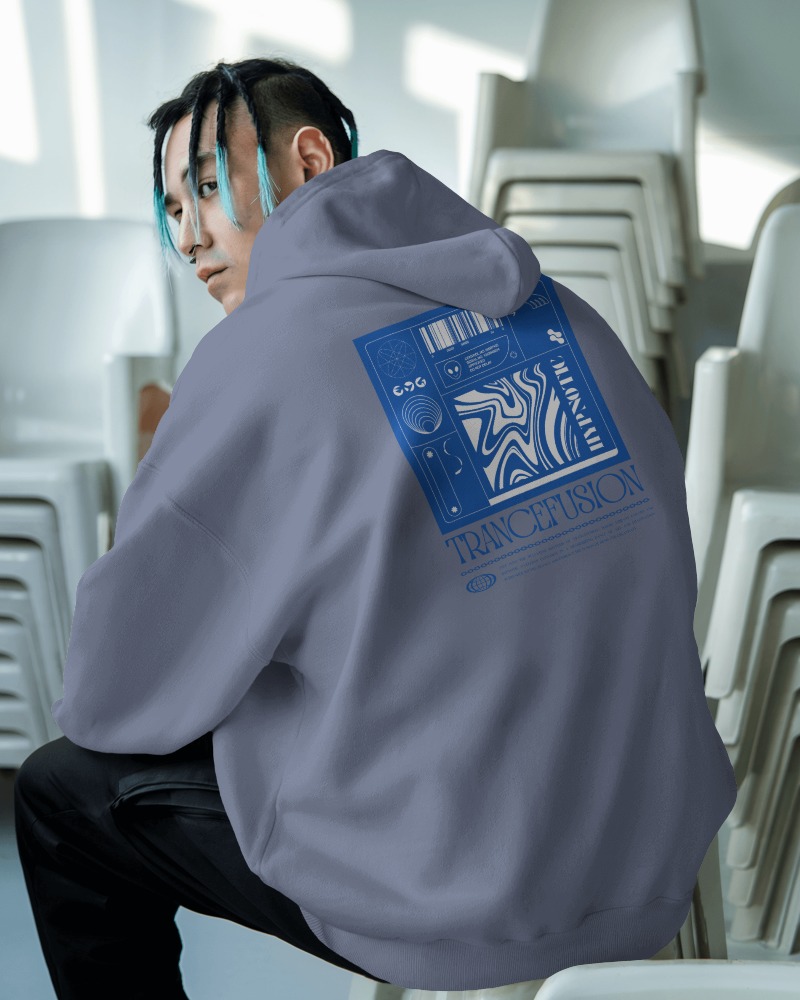 Urban Streetwear Hoodie Mockup Male Model In Muted Gray Trancefusion Design Sitting Amidst Stacked Chairs Edgy Modern Vibe