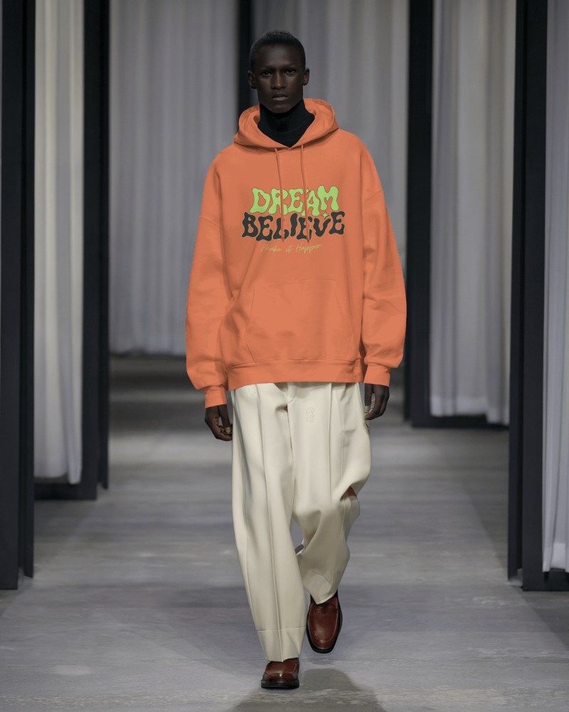 Runway Walk Hoodie Mockup Male Model In Bold Purple Streetwear Contrasting Neutral Trousers And Dark Background