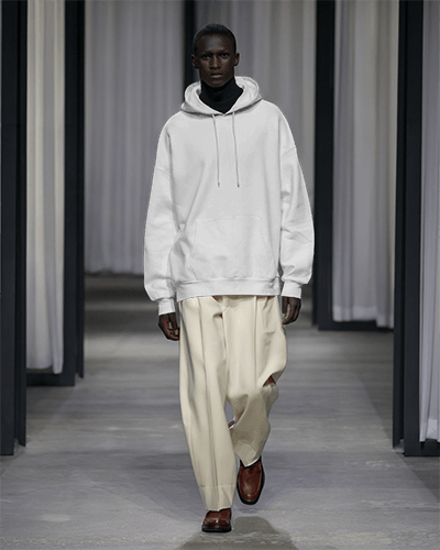 Runway Walk Hoodie Mockup Male Model In Bold Purple Streetwear Contrasting Neutral Trousers And Dark Background