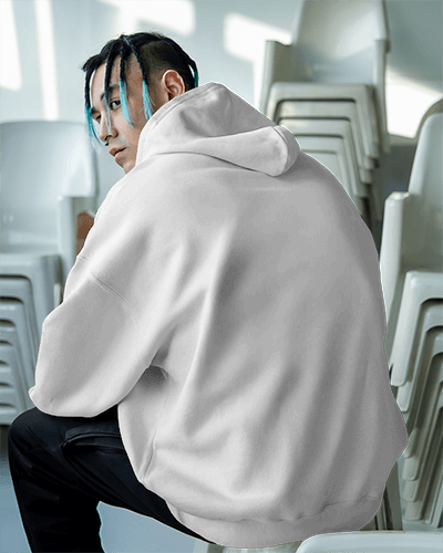 Urban Streetwear Hoodie Mockup Male Model In Muted Gray Trancefusion Design Sitting Amidst Stacked Chairs Edgy Modern Vibe