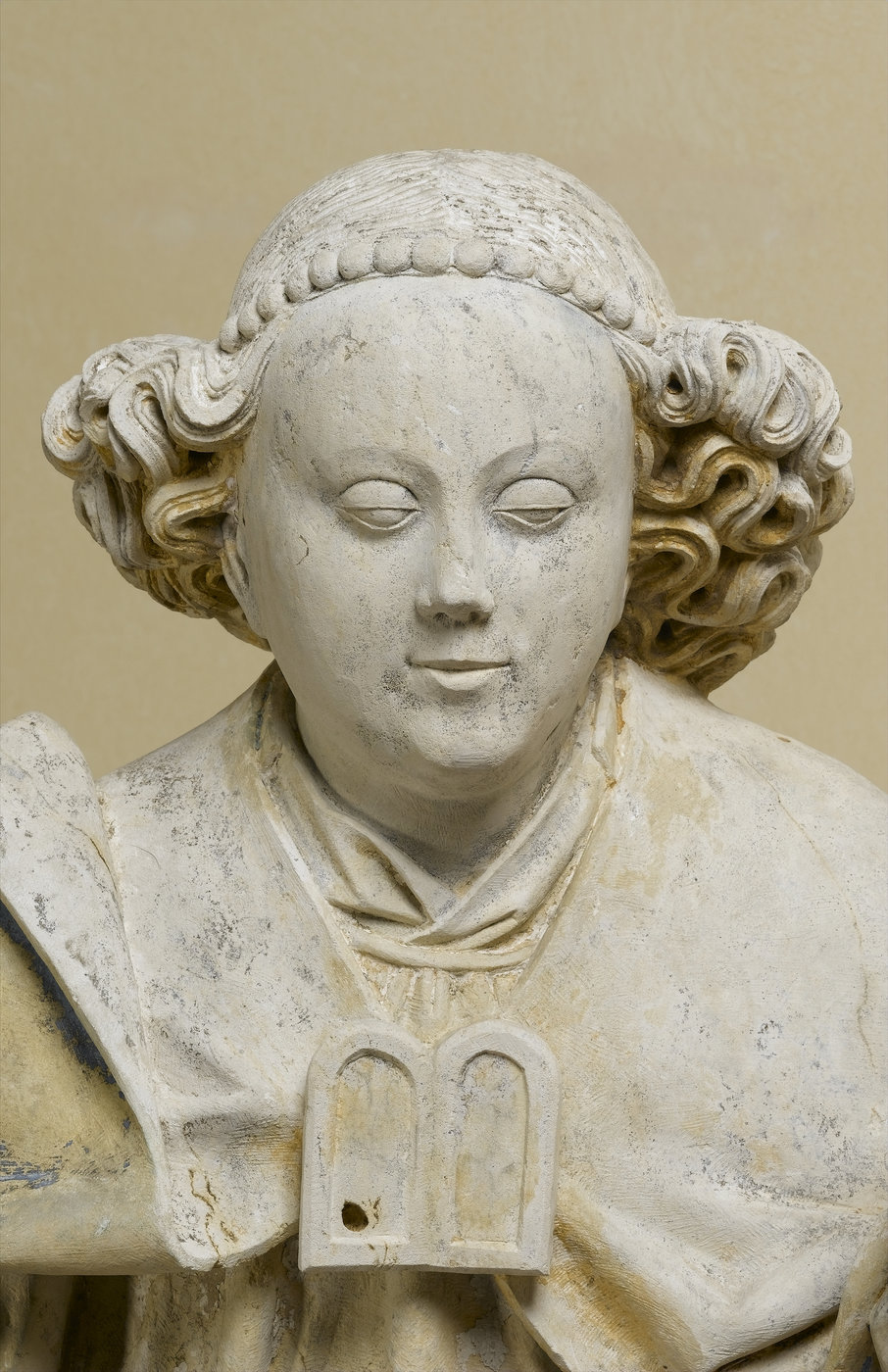 Sculpture en pierre de l'ange Gabriel, présentant des traces de polychromie, détail du buste. Vue de face sur fond neutre.