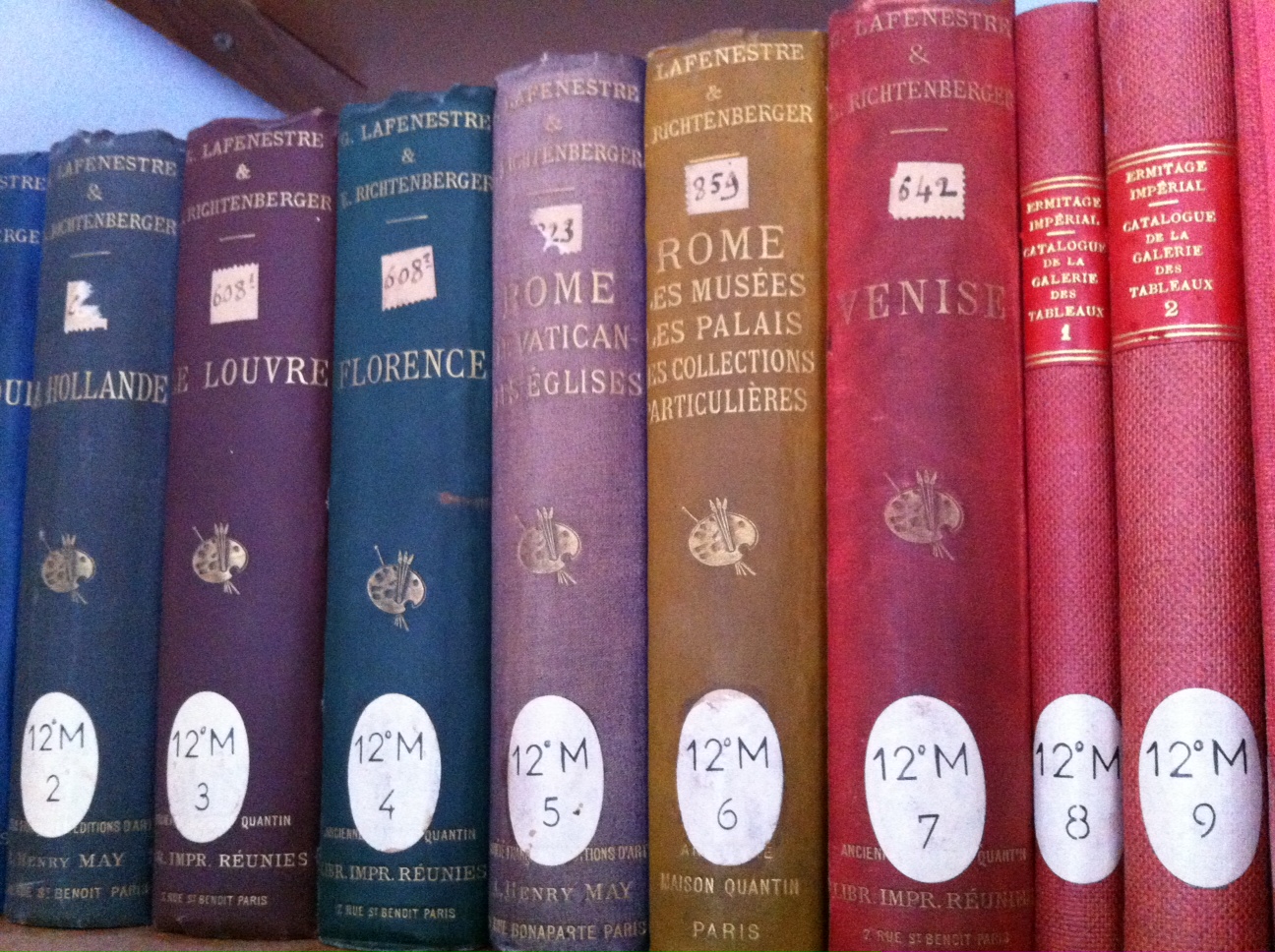 Row of printed and labeled books. Only the colored spines are visible. Three-quarter view.