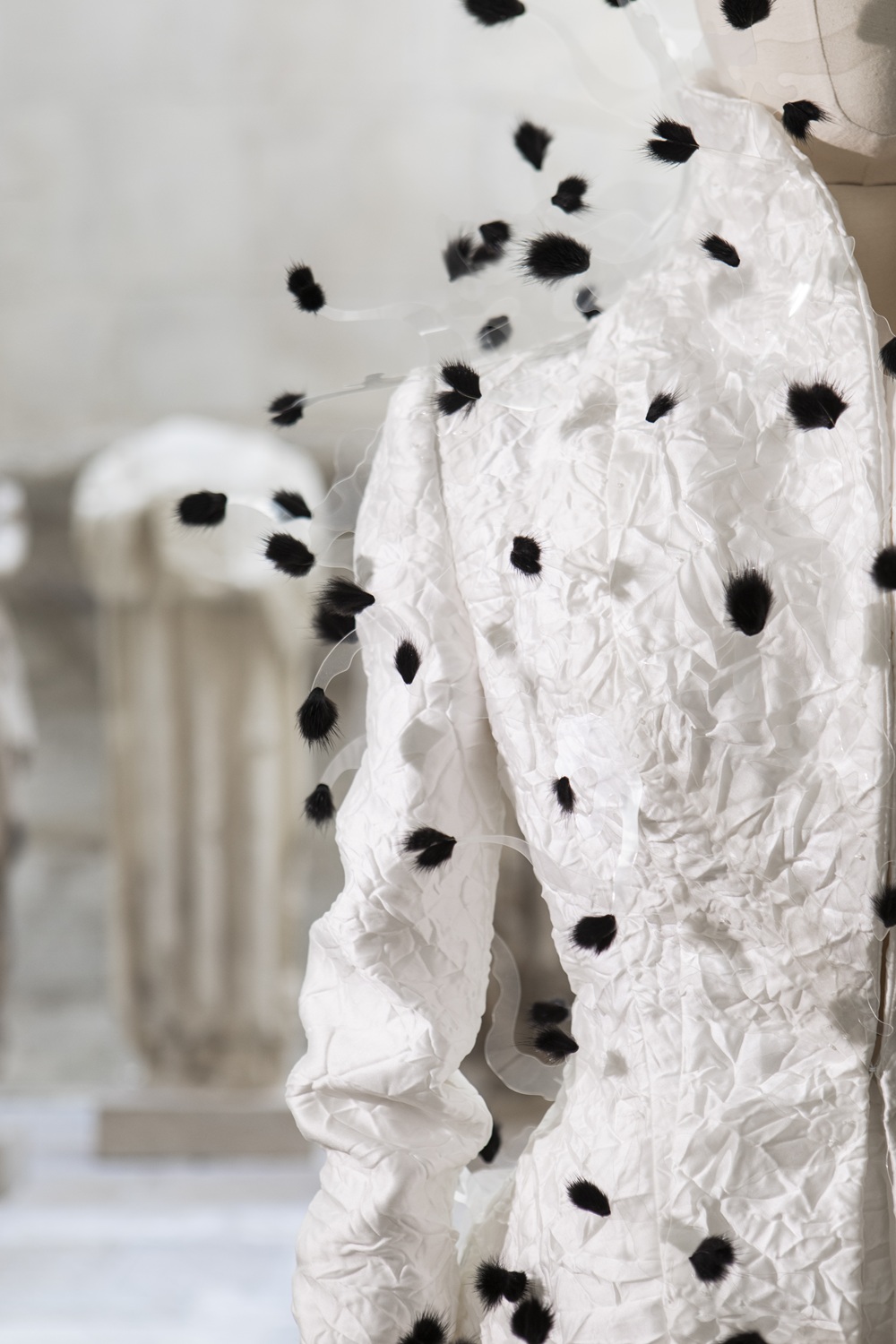 Détail d'une veste blanche avec tressage textile noir. Vue du col et d'une épaule.