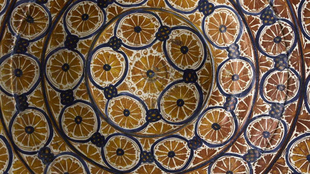 Détail de plat rond en céramique émaillée à reflet métallique orné de motifs de tranches d’oranges. Vue de face.