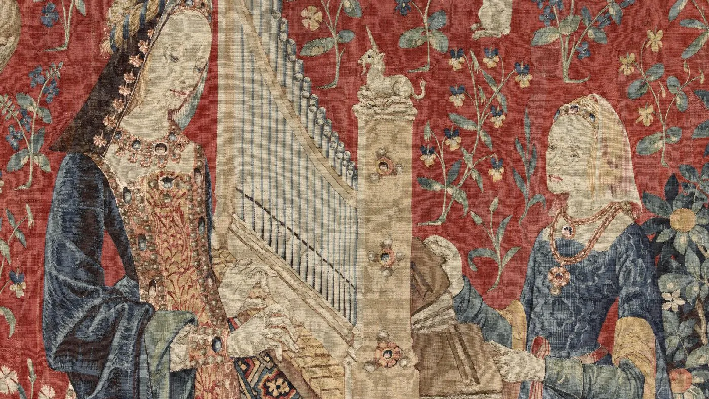 Tapisserie : deux femmes jouant de l’orgue sur fond rouge orné de fleurs et d’animaux. Vue de face.