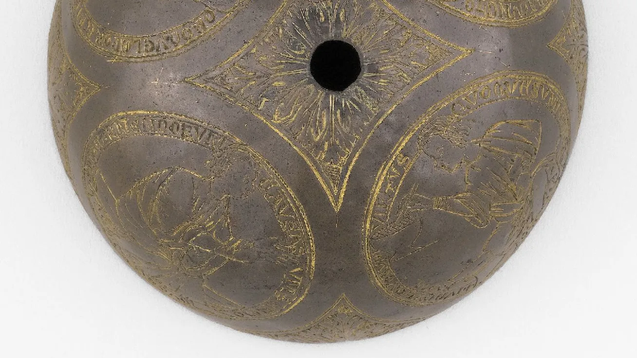 Demi-sphère en métal gravée de personnages de profil dans quatre médaillons. Photographie de face.