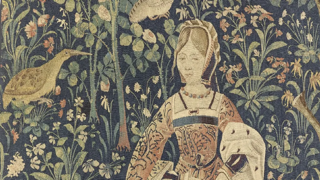 Détail d'une tapisserie représentant une femme en train de broder dans un décor végétal.