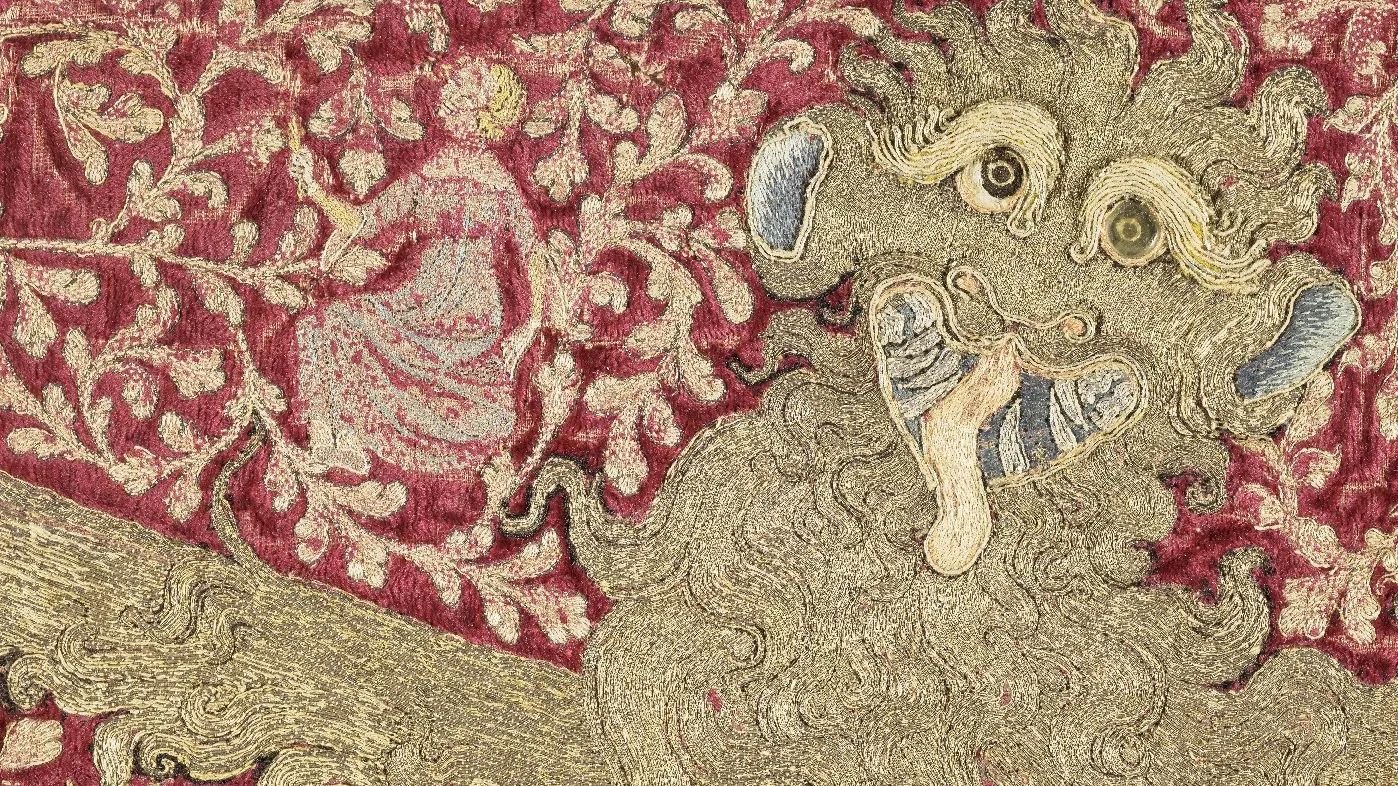Broderie représentant une tête de léopard stylisée sur fond de feuillage animé d’un personnage féminin. Photographie de face.
