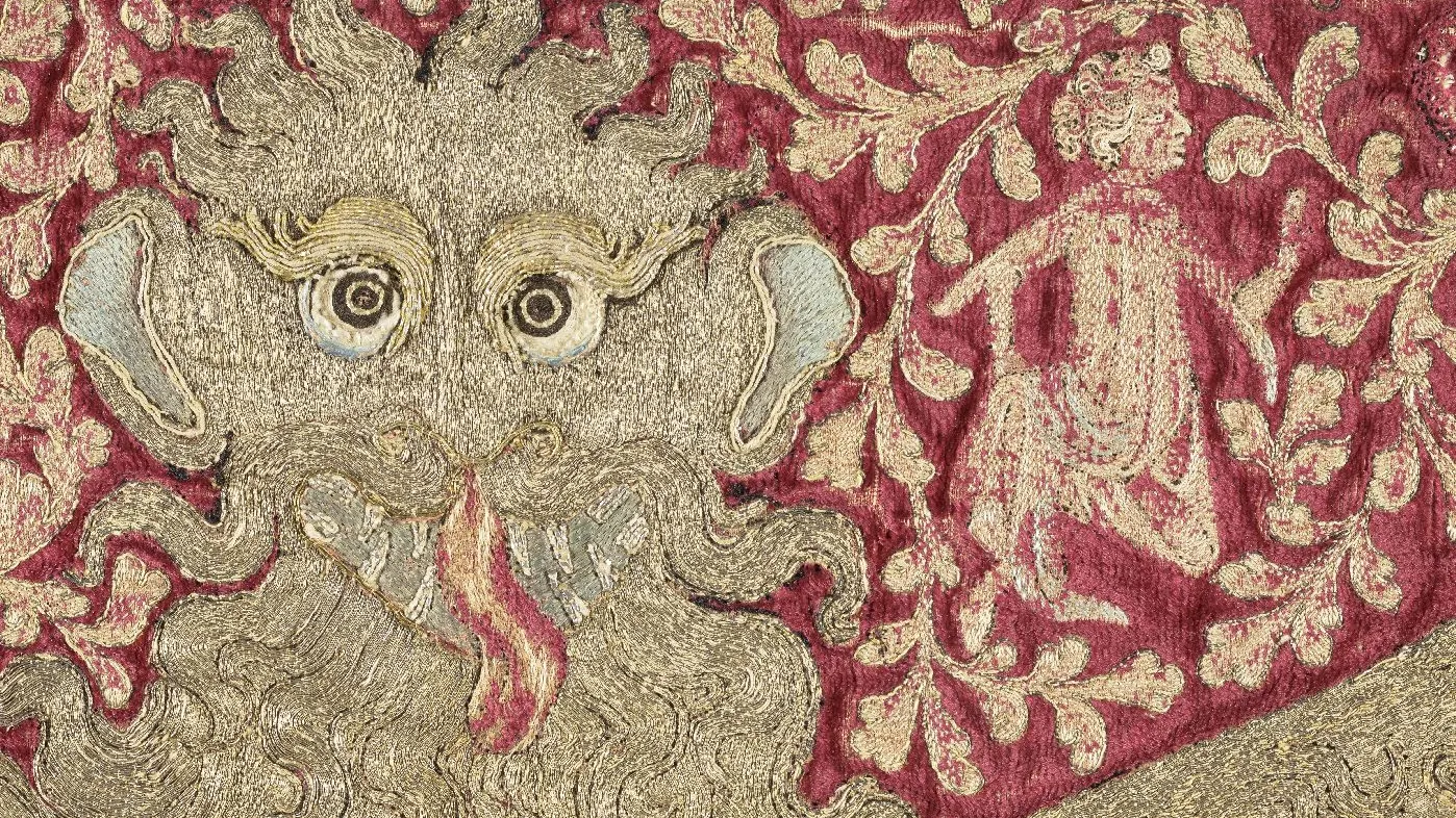 Broderie représentant une tête de léopard stylisée sur un fond de feuillage animé par un personnage. Photographie de face.
