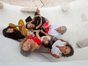 Six femmes sont vues de haut, le visage tourné vers l'appareil photo. Quatre sont assises et deux debout dans un décor minéral.