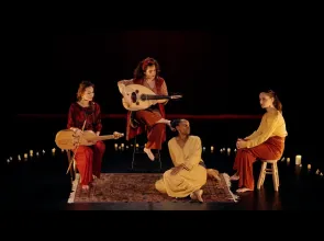 Quatre femmes sont sur scène, sur fond noir. Deux jouent d'un instrument. Elles sont assises dans un demi-cercle de bougies. 