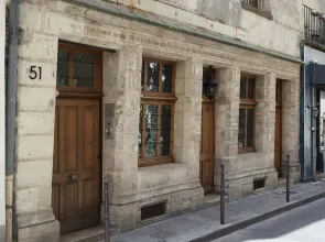 Façade en pierre d'une maison identifiée par le numéro 51. Murs en pierre, porte et fenêtres en bois. Photographie prise de la rue de trois-quarts. 