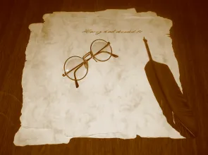 Photographie d'un parchemin sur lequel sont posées une paire de lunette et une plume
