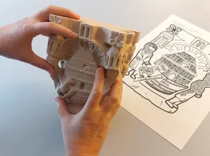 Photo de deux mains qui touchent la reproduction d'un chapiteau médiéval