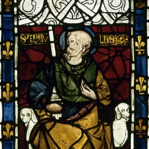 Vitrail représentant un homme barbu en vêtement bleu, jaune et verre. À ses pieds : deux chiens de type lévrier. Bordure de fleurs de lis.