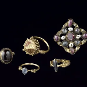 Cuatro anillos y un broche decorados con piedras. Fotografía sobre fondo neutro.