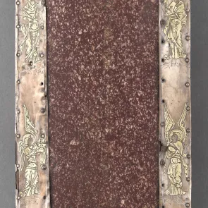 Objet rectangulaire formé d’une plaque de porphyre pourpre entourée d’argent gravé de motifs religieux. Photographie de face.