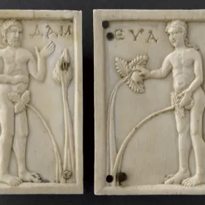 Dos plaquitas de marfil tallado que representan a Adán y Eva de perfil, desnudos, ocultos por una hoja de parra. Vista frontal.