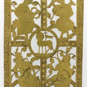 Perforated metal plaque: central lamb surrounded by four figures carrying jugs, framed by inscriptions. Front view.
