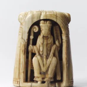 Carved ivory object depicting a seated figure under an arch holding a crozier and a parchment. Front view.