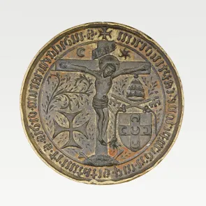 Circular metal seal matrix depicting Christ on the cross, surrounded by inscriptions and heraldic motifs. Front view.