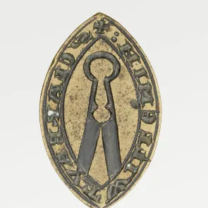 Objet métallique gravé, de forme ovale, orné d’une inscription. Vue de face.