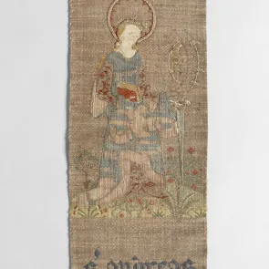 Bande de tissu brodé représentant de haut en bas : bas d’un personnage, femme auréolée avec épée et homme auréolé en buste, séparés par des inscriptions. Vue de face.