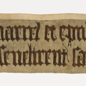 Fragment of a tapestry adorned with two lines of inscriptions in Gothic style. Front view.