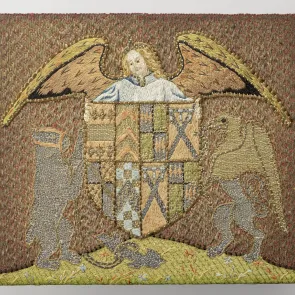 Bordado que representa a un ángel sobre un escudo heráldico sostenido por un oso y un grifo. Vista frontal.
