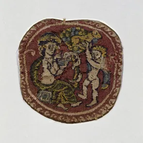 Médaillon tissé représentant une femme qui tend une coupe à un serpent enroulé autour d’un arbre. Un homme attrape un agneau. Vue de face.
