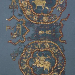 Fragment of blue fabric embroidered with red and gold: medallions featuring a human-headed animal and a rider holding a falcon and a rabbit. Front view.