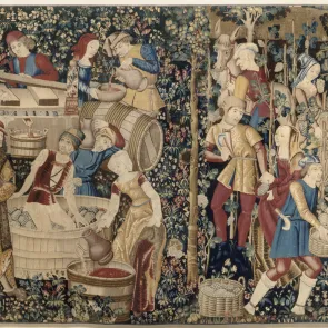 Tapisserie représentant plusieurs épisodes des vendanges. De nombreux personnages en tenue seigneuriale évoluent dans un décor de millefleurs. Vue de face. 