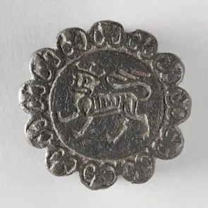 Objet rond métallique gravé d’un animal couronné entouré d’un motif végétal. Vue de face.