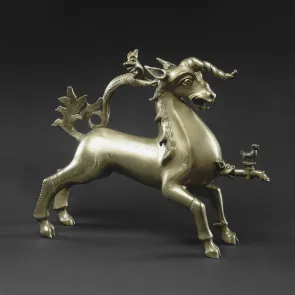 Objeto metálico en forma de unicornio con un dragón en el lomo. Vista de tres cuartos sobre fondo gris.