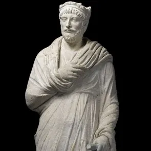 Escultura en piedra que representa a un hombre vestido con una toga antigua, con la mano izquierda plegada y barba corta. Vista frontal.