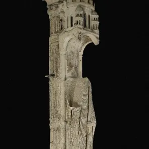 Colonne de pierre sculptée : personnage fragmentaire dans un décor architectural. Vue de trois quarts.