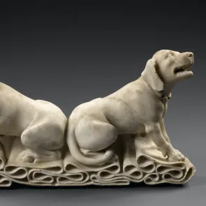 Sculpture en pierre : deux chiens assis dos à dos sur un tissu plissé, regardant vers le ciel. Photographie de profil.