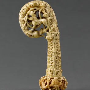 Crosseron en ivoire sculpté : volute en tête de dragon avec rinceaux habités d’un lion. Vue de face.