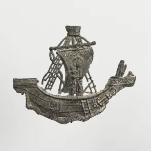 Objeto de plomo: barco con una inscripción en la vela que transporta una Virgen con el Niño. Vista frontal.